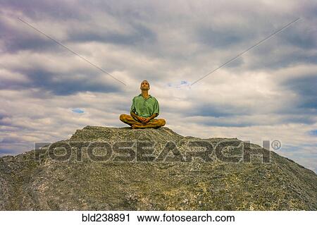 Stock Image - Man meditating on rock under clouds. Fotosearch