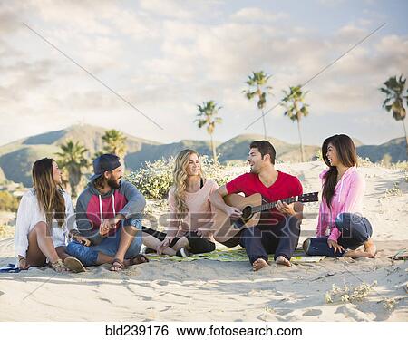 Stock Photograph - Man playing guitar for friends at beach. Fotosearch
