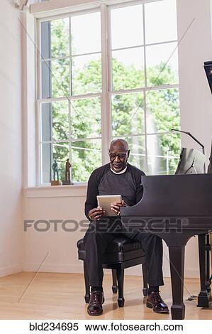 Man sitting at piano using digital tablet near window View Large Photo Image Stock Photography - Man sitting at piano using digital tablet near window. Fotosearch