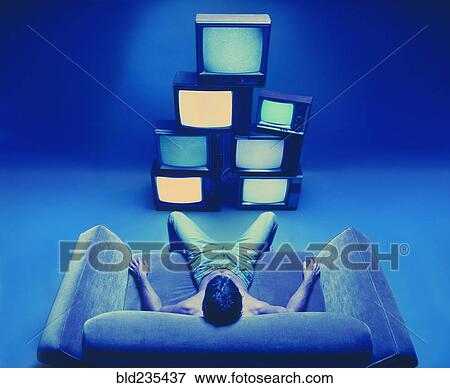 Stock Photo - Man sitting on loveseat watching stack of televisions. Fotosearch