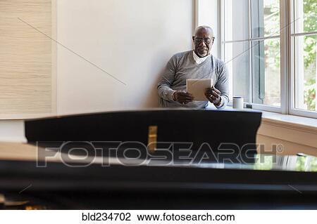 Man using digital tablet near window behind piano View Large Photo Image Stock Image - Man using digital tablet near window behind piano. Fotosearch