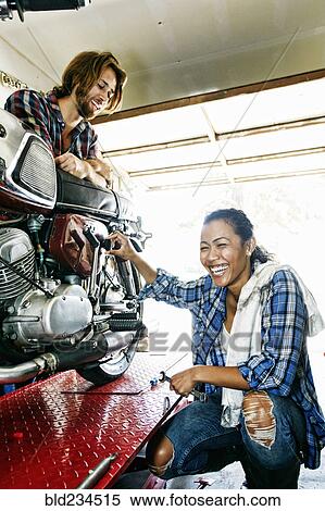 Man watching laughing woman repairing motorcycle in garage View Large Photo Image Stock Photography - Man watching laughing woman repairing motorcycle in garage. Fotosearch