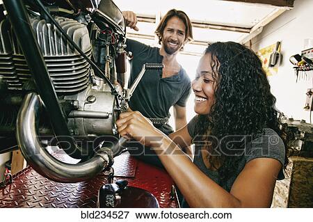 Man watching woman repairing motorcycle in garage View Large Photo Image Stock Photo - Man watching woman repairing motorcycle in garage. Fotosearch
