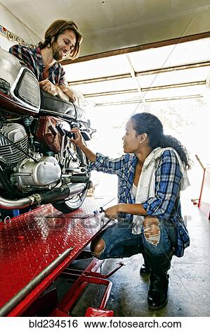 Stock Photograph - Man watching woman repairing motorcycle in garage. Fotosearch