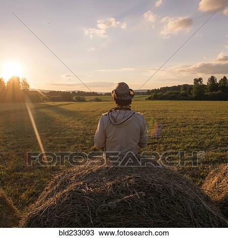 Stock Image - Mari man sitting on hay bale at sunset. Fotosearch