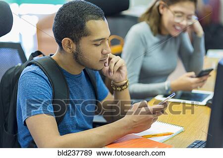 Mixed Race boy and girl texting on cell phones in library View Large Photo Image Stock Photo - Mixed Race boy and girl texting on cell phones in library. Fotosearch