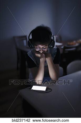 Stock Image - Mixed Race boy listening to cell phone with headphones. Fotosearch
