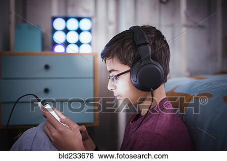 Mixed Race boy listening to cell phone with headphones View Large Photo Image Stock Photo - Mixed Race boy listening to cell phone with headphones. Fotosearch