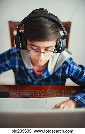 Stock Image - Mixed Race boy listening to laptop with headphones. Fotosearch
