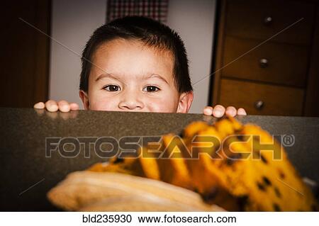 Stock Image - Mixed Race boy looking at cake on counter. Fotosearch