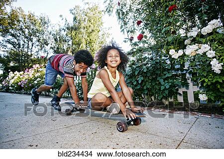 Mixed Race boy pushing sister on skateboard on sidewalk View Large Photo Image Picture - Mixed Race boy pushing sister on skateboard on sidewalk. Fotosearch