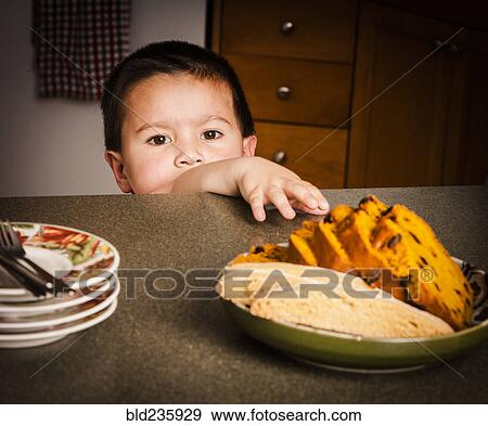 Mixed Race boy reaching for cake on counter View Large Photo Image Stock Photo - Mixed Race boy reaching for cake on counter. Fotosearch