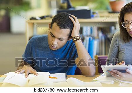 Stock Image - Mixed Race boy reading book in library. Fotosearch