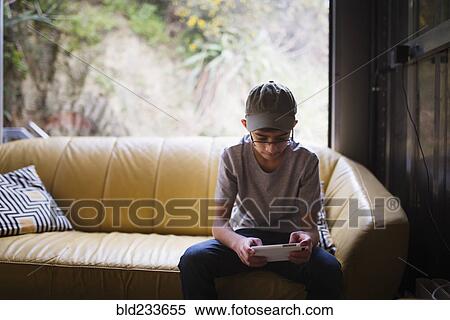 Stock Photography - Mixed Race boy sitting on sofa near window texting on cell phone . Fotosearch
