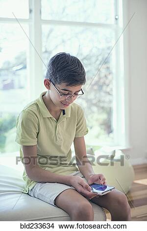 Picture - Mixed Race boy texting on cell phone near window. Fotosearch