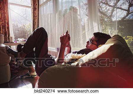 Picture - Mixed Race boy texting on cell phone near window. Fotosearch