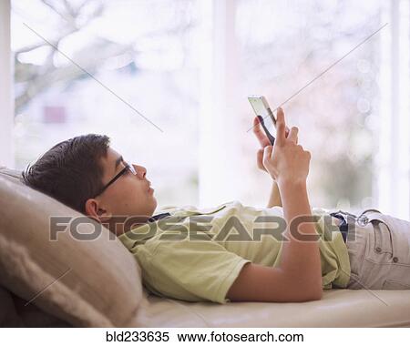 Stock Photography - Mixed Race boy texting on cell phone near window. Fotosearch