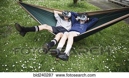 Stock Photo - Mixed Race brother and sister in hammock wearing virtual reality goggles. Fotosearch