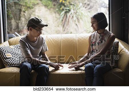 Picture - Mixed Race brother and sister playing finger game on sofa near window. Fotosearch