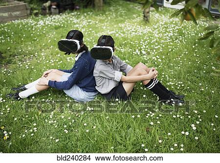 Mixed Race brother and sister sitting in grass wearing virtual reality goggles View Large Photo Image Picture - Mixed Race brother and sister sitting in grass wearing virtual reality goggles. Fotosearch