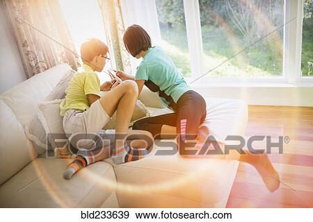 Stock Photo - Mixed Race brother and sister texting on cell phone near window. Fotosearch