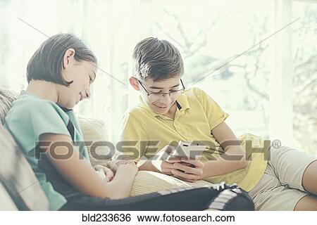 Mixed Race brother and sister texting on cell phone near window View Large Photo Image Stock Photograph - Mixed Race brother and sister texting on cell phone near window. Fotosearch