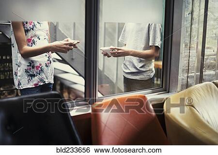 Stock Photograph - Mixed Race brother and sister texting on cell phones behind window. Fotosearch