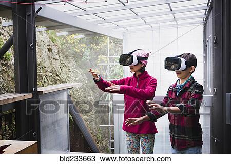 Stock Image - Mixed Race brother and sister using virtual reality goggles on veranda. Fotosearch