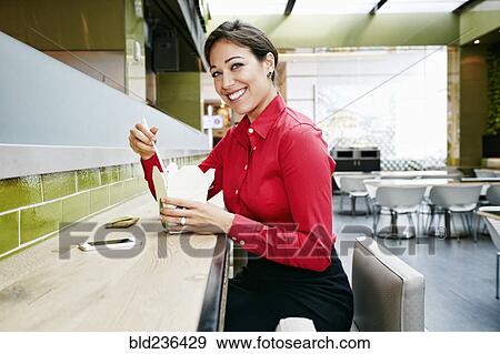 Stock Photo - Mixed Race businesswoman eating food with chopsticks in food court. Fotosearch
