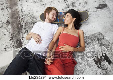 Picture - Mixed Race couple laying on rooftop with skateboard. Fotosearch
