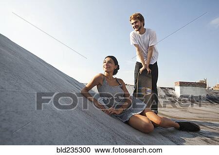Stock Image - Mixed Race couple on rooftop with skateboard. Fotosearch