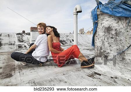 Mixed Race couple sitting back to back on rooftop with skateboard View Large Photo Image Stock Image - Mixed Race couple sitting back to back on rooftop with skateboard. Fotosearch