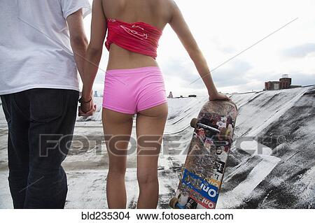 Picture - Mixed Race couple standing on rooftop with skateboard. Fotosearch