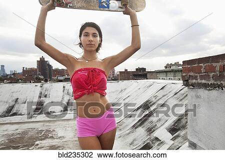 Stock Image - Mixed Race couple woman on rooftop holding skateboard. Fotosearch