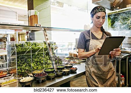 Stock Photo - Mixed Race food court worker using digital tablet. Fotosearch