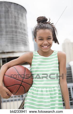 Stock Image - Mixed Race girl holding basketball in city. Fotosearch