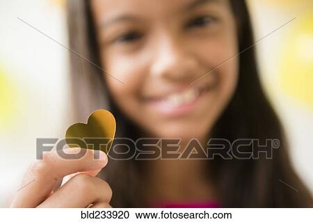 Stock Image - Mixed Race girl holding golden heart-shape confetti. Fotosearch