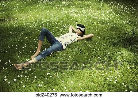 Stock Photograph - Mixed Race girl laying in grass wearing virtual reality goggles. Fotosearch