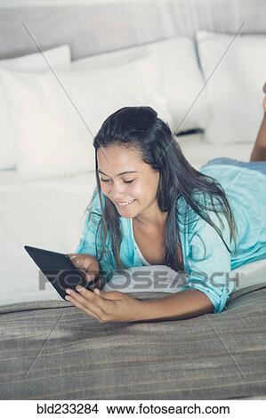 Mixed Race girl laying on bed reading digital tablet View Large Photo Image Picture - Mixed Race girl laying on bed reading digital tablet. Fotosearch