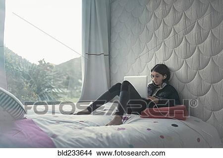 Picture - Mixed Race girl laying on bed using laptop. Fotosearch