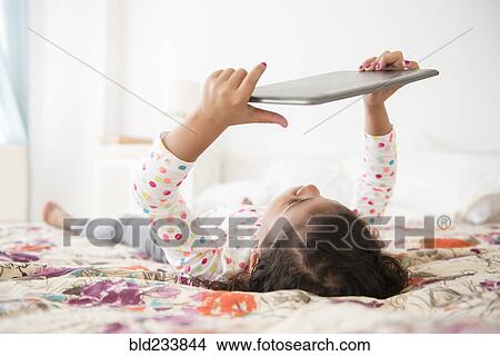 Mixed Race girl laying on bed using digital tablet View Large Photo Image Picture - Mixed Race girl laying on bed using digital tablet. Fotosearch