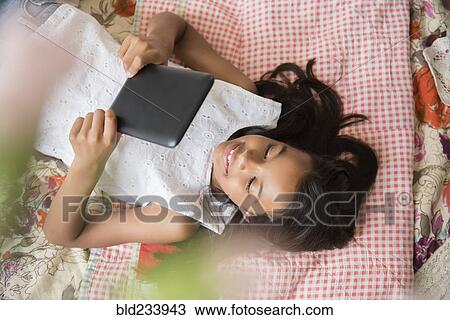 Mixed Race girl laying on bed using digital tablet View Large Photo Image Stock Image - Mixed Race girl laying on bed using digital tablet. Fotosearch