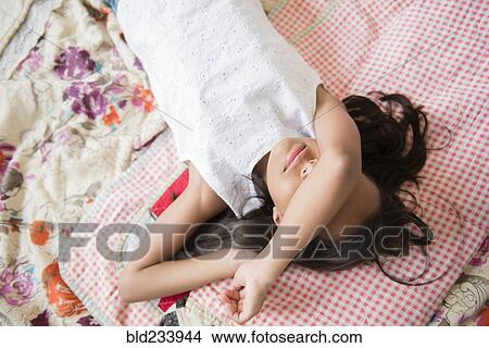 Picture - Mixed Race girl laying on bed with arm covering face. Fotosearch