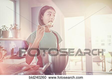 Stock Image - Mixed Race girl licking cookie dough on spoon. Fotosearch
