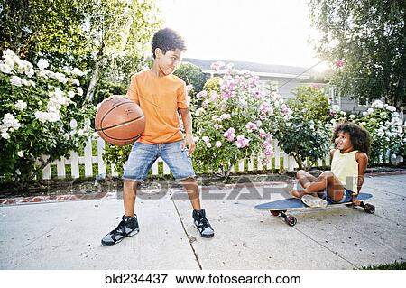 Mixed Race girl on skateboard watching brother dribbling basketball View Large Photo Image Stock Photo - Mixed Race girl on skateboard watching brother dribbling basketball. Fotosearch