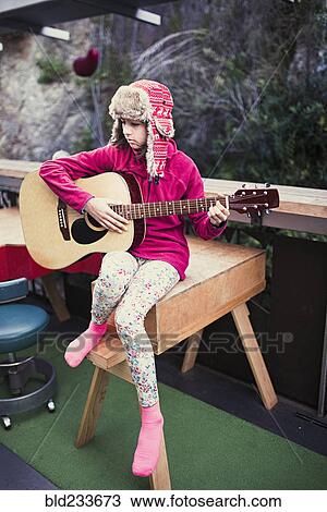 Stock Image - Mixed Race girl playing acoustic guitar on veranda. Fotosearch
