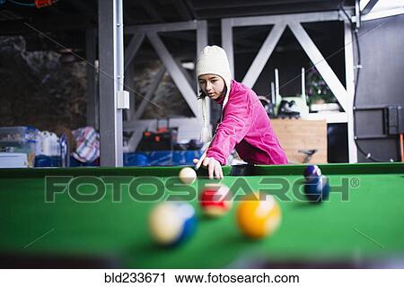 Stock Image - Mixed Race girl playing at pool table. Fotosearch