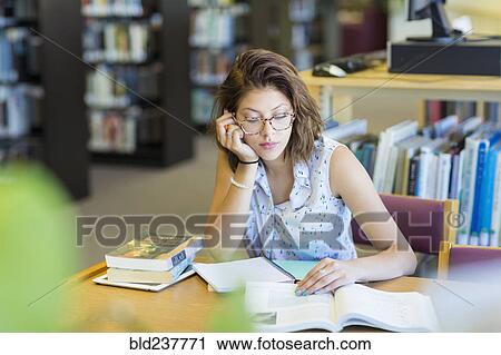 Stock Image - Mixed Race girl reading book in library. Fotosearch