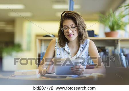 Stock Image - Mixed Race girl reading digital tablet in library. Fotosearch