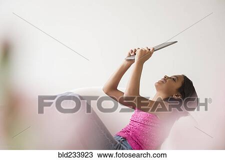 Stock Image - Mixed Race girl relaxing in armchair using digital tablet. Fotosearch